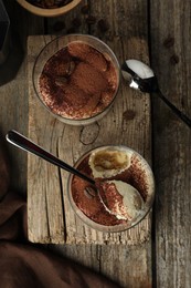 Photo of Delicious tiramisu in glasses, spoons and coffee beans on wooden table, top view
