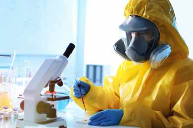 Photo of Scientist in chemical protective suit dripping blood sample into Petri dish at laboratory. Virus research