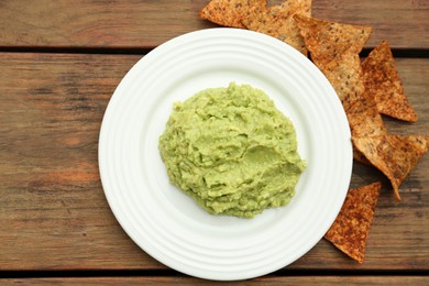 Photo of Delicious guacamole made of avocados and nachos on wooden table, flat lay