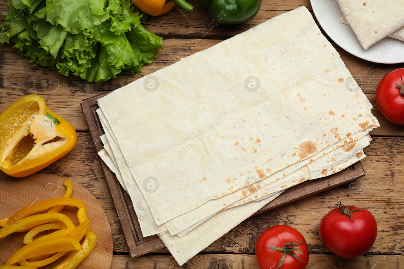 Photo of Delicious Armenian lavash and fresh vegetables on wooden table, flat lay