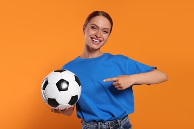 Happy fan showing football ball on orange background