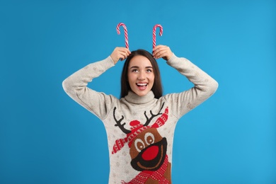 Young woman in Christmas sweater holding candy canes on blue background