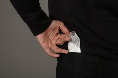 Photo of Drug dealer taking bag with cocaine out of pocket on dark background, closeup. Space for text