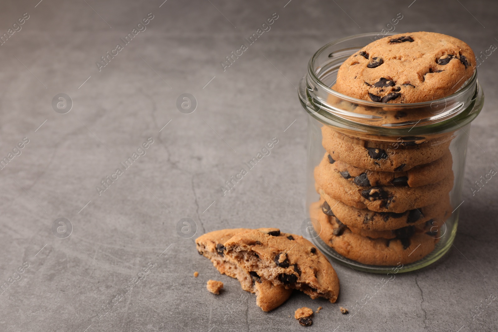 Glass jar with delicious chocolate chip cookies on grey table. Space for text Photo of Glass jar with delicious chocolate chip cookies on grey table. Space for text