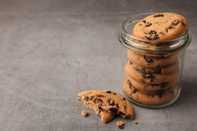 Photo of Glass jar with delicious chocolate chip cookies on grey table. Space for text