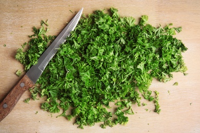 Photo of Chopped parsley and knife on wooden background, top view