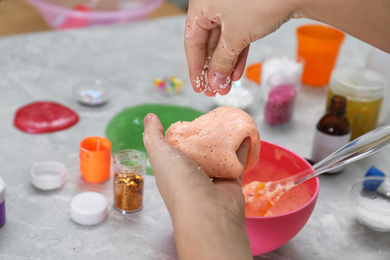 Photo of Little girl adding decorative balls to homemade slime toy at table, closeup