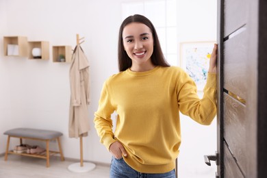 Photo of Happy woman standing near door, space for text. Invitation to come indoors
