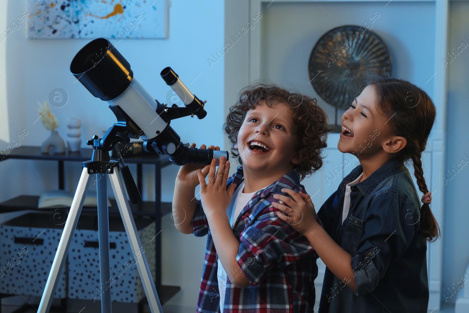 Photo of Cute little children using telescope to look at stars in room