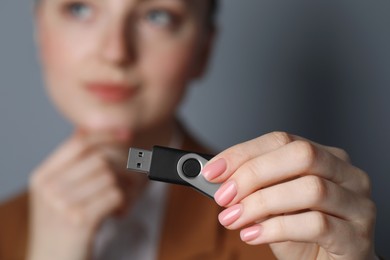 Photo of Woman holding usb flash drive against grey background, focus on hand