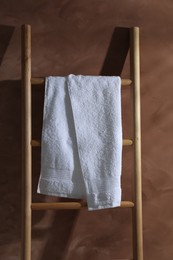 Photo of Clean towel on wooden decorative ladder against brown background