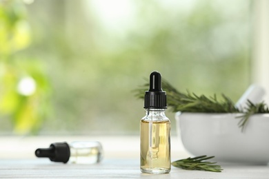 Photo of Bottle of rosemary essential oil on white wooden table against blurred background. Space for text