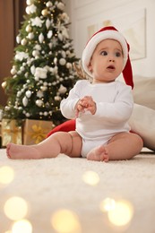 Photo of Baby wearing Santa hat on floor in room decorated for Christmas