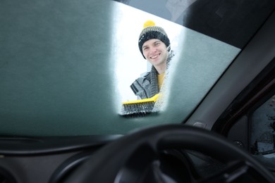 Photo of Man cleaning snow from car windshield, view from inside