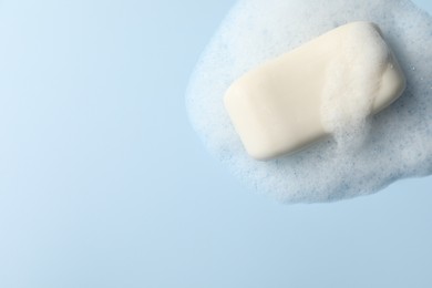 Photo of Soap with fluffy foam on light blue background, top view. Space for text