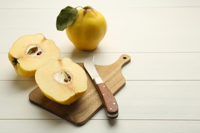 Photo of Tasty ripe quince fruits and knife on white wooden table, space for text