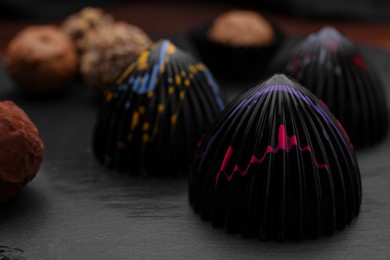 Photo of Different tasty chocolate candies on slate plate, closeup