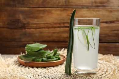 Photo of Tasty aloe juice in glass and cut fresh leaves on wooden table, space for text