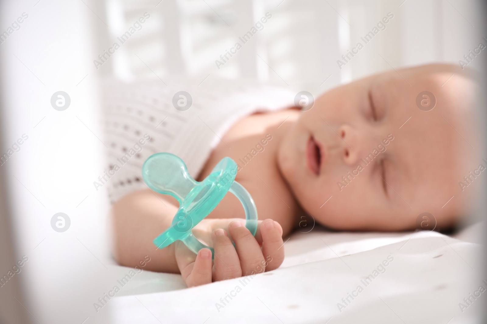 Photo of Cute little baby sleeping in crib, focus on hand with pacifier