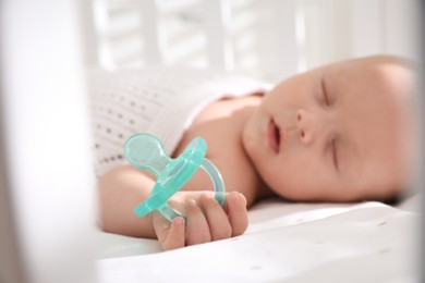 Photo of Cute little baby sleeping in crib, focus on hand with pacifier