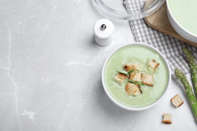 Photo of Bowl of delicious asparagus soup served on light grey table, flat lay. Space for text