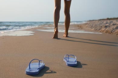 Photo of Woman left her beach slippers and walking barefoot on sandy seashore, closeup