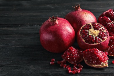 Photo of Ripe pomegranates and seeds on wooden background, space for text