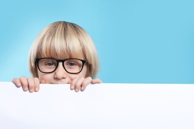 Photo of Cute little boy in glasses with blank board on light blue background, space for text