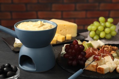 Photo of Fondue with tasty melted cheese, fork and different snacks on black table