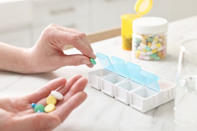 Photo of Woman with pills, organizer and glass of water at white marble table, closeup