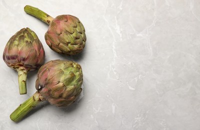 Photo of Fresh raw artichokes on grey marble table, flat lay. Space for text