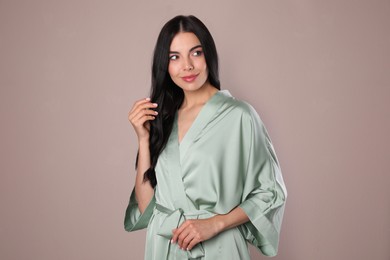 Photo of Pretty young woman in light silk robe on beige background