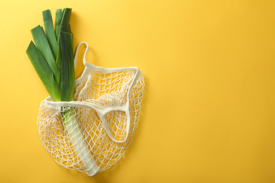 Photo of Net bag with leek on yellow background, top view. Space for text