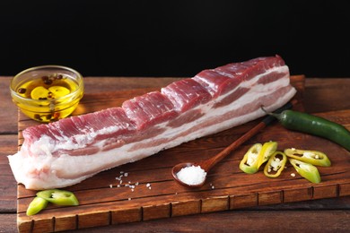 Photo of Piece of raw pork belly, green chili pepper and salt on wooden table