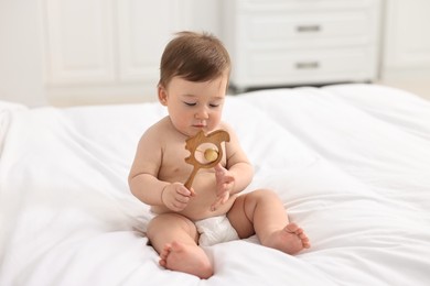 Photo of Cute baby boy with wooden rattle on bed at home