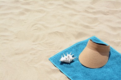 Towel, straw visor cap and seashell on sand, space for text. Beach accessories