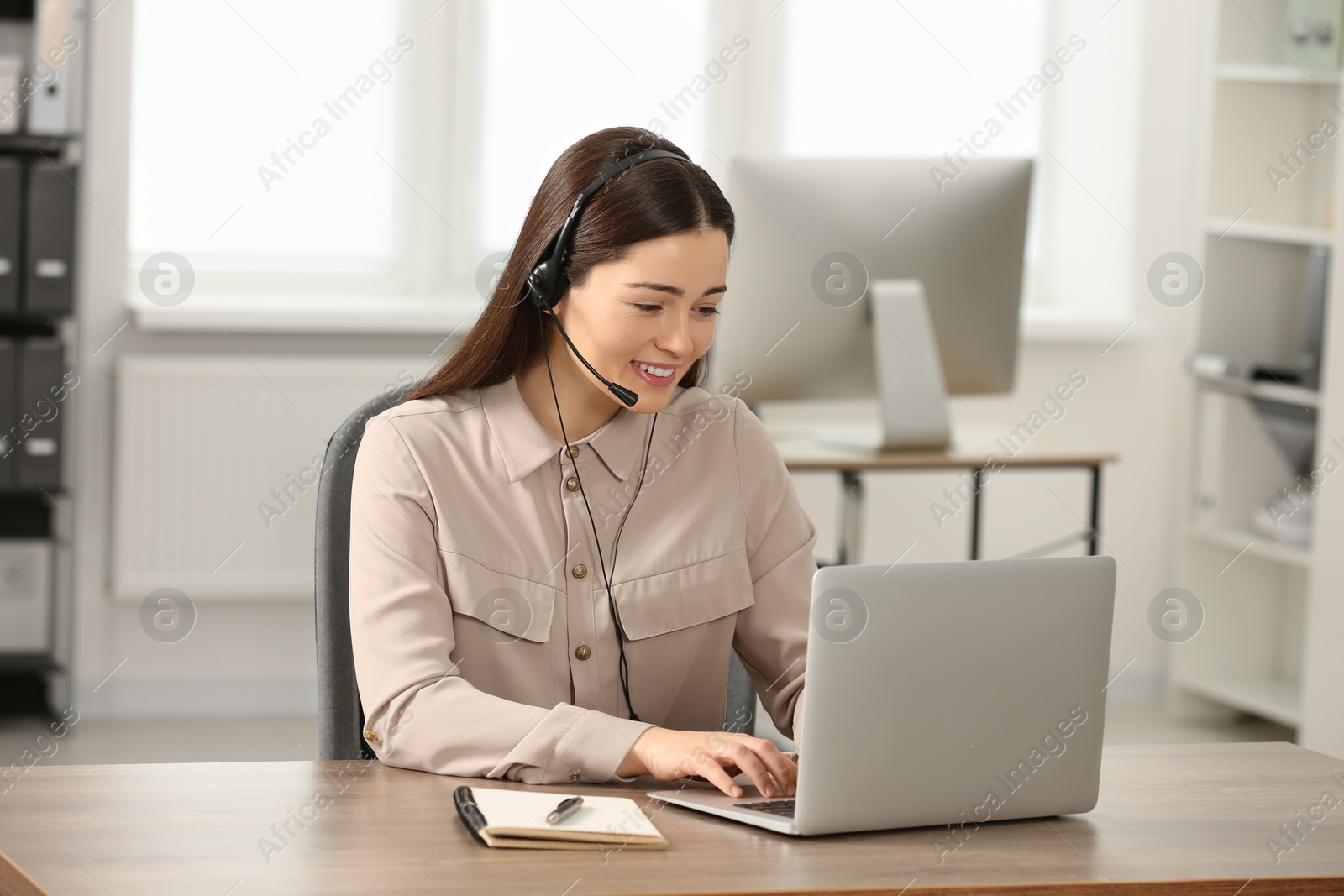 Photo of Hotline operator with headset working on laptop in office