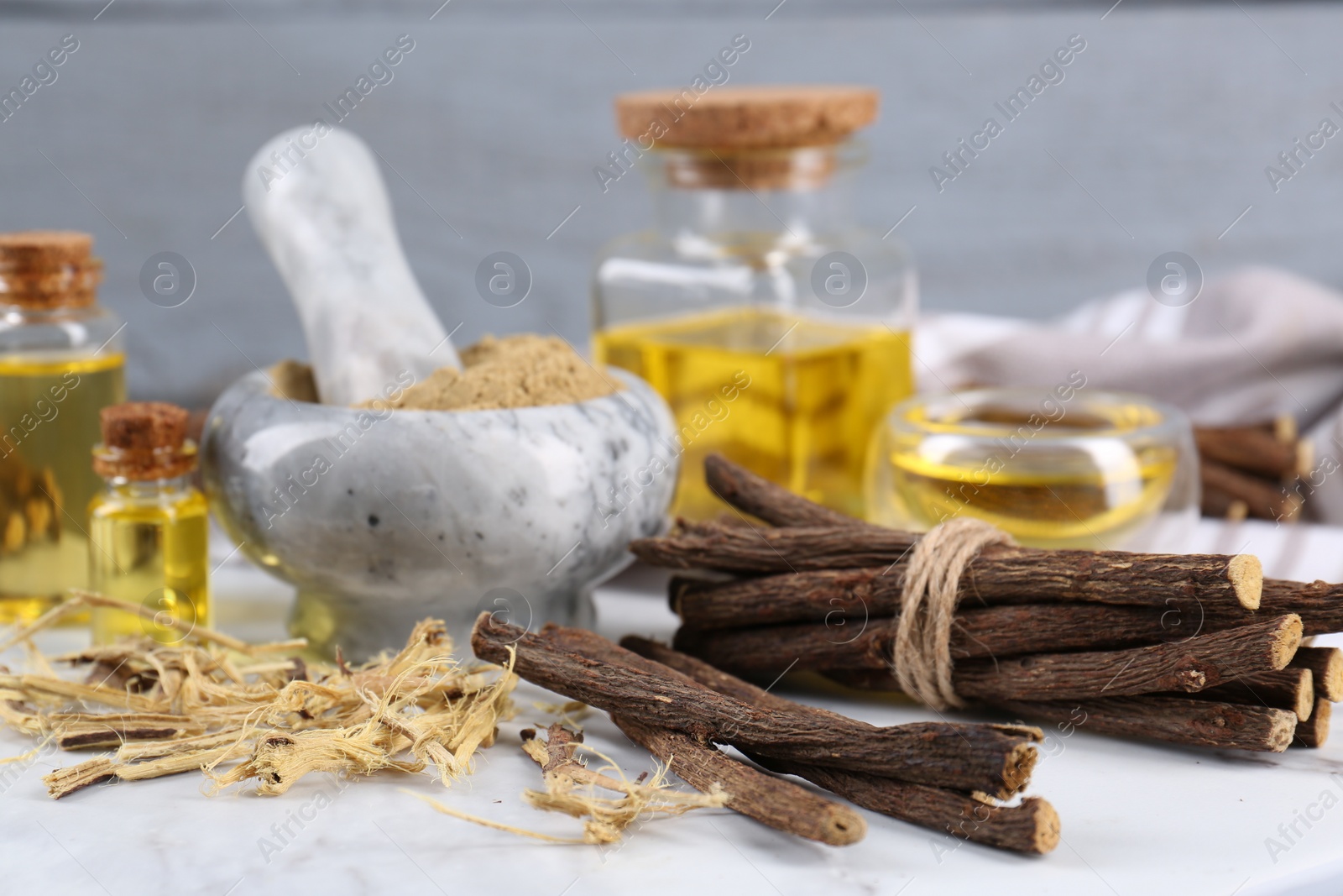 Photo of Dried sticks of licorice roots, powder and essential oil on white table, closeup