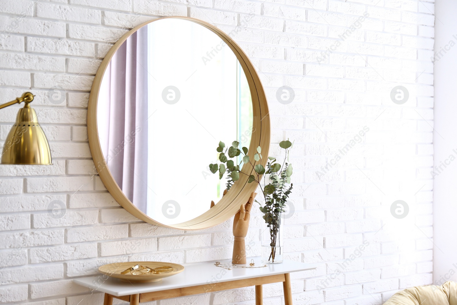 Photo of Big round mirror, table with jewelry and decor near brick wall in hallway interior