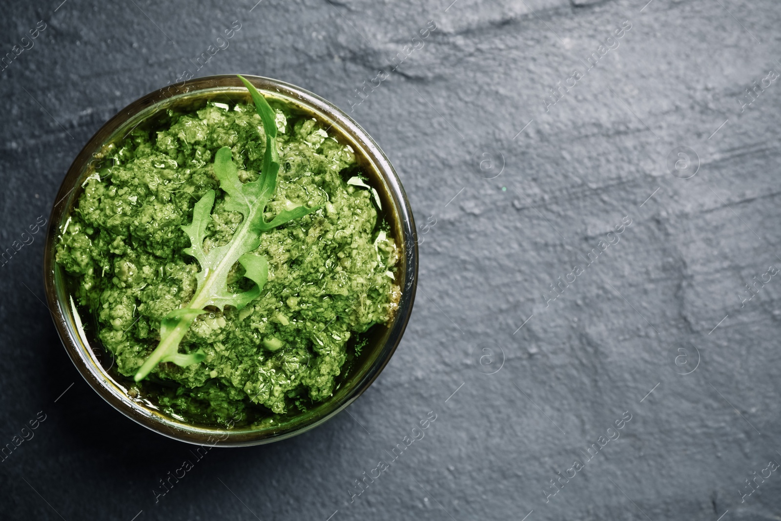 Photo of Bowl with tasty arugula pesto on black table, top view. Space for text