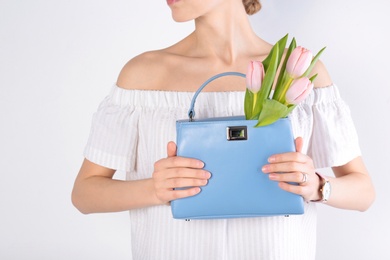 Photo of Stylish woman with handbag and spring flowers against light background, closeup