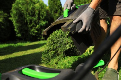 Man removing grass out of lawn mower box in garden, closeup