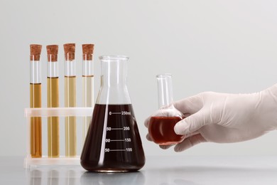 Photo of Scientist holding round bottom flask with brown liquid near laboratory glassware on light background, closeup