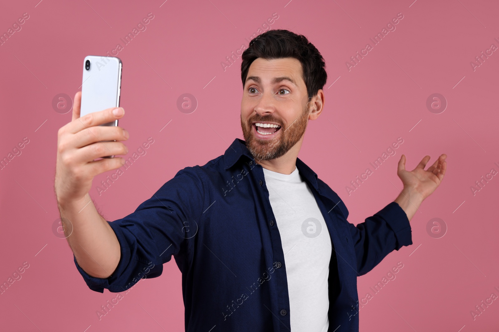 Photo of Smiling man taking selfie with smartphone on pink background