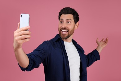 Smiling man taking selfie with smartphone on pink background