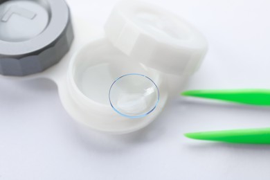 Case with contact lens and tweezers on white background, closeup