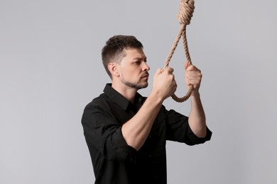 Depressed man with rope noose on light background