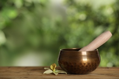 Photo of Golden singing bowl, mallet and flower on wooden table outdoors, space for text