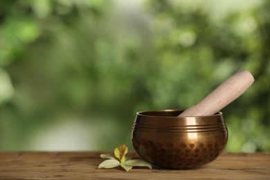 Golden singing bowl, mallet and flower on wooden table outdoors, space for text