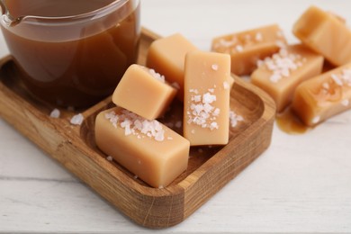 Yummy caramel candies, sauce and sea salt on white wooden table, closeup